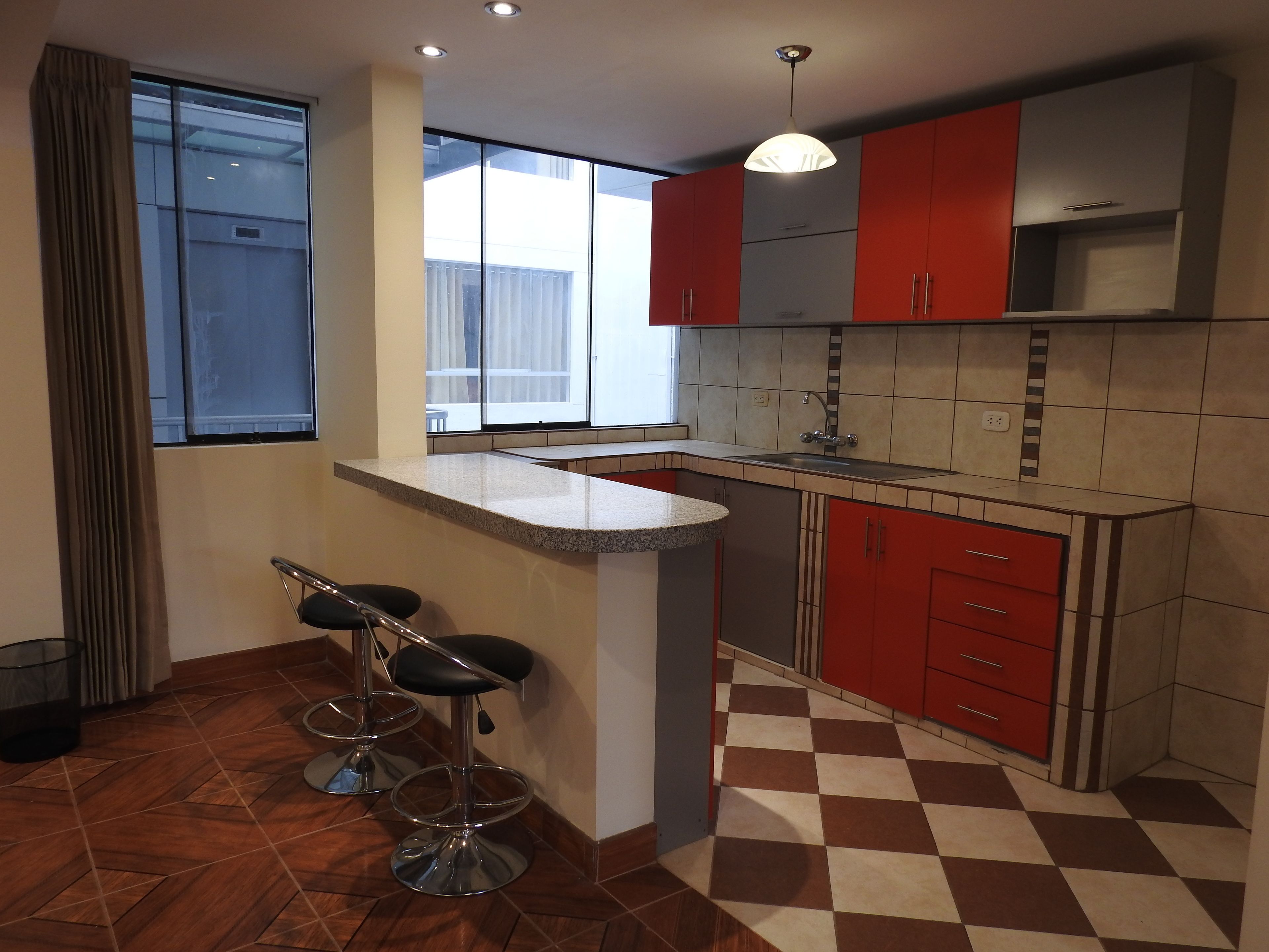 Una cucina con pavimento a scacchi, una zona bar con sgabelli e mobili rossi.