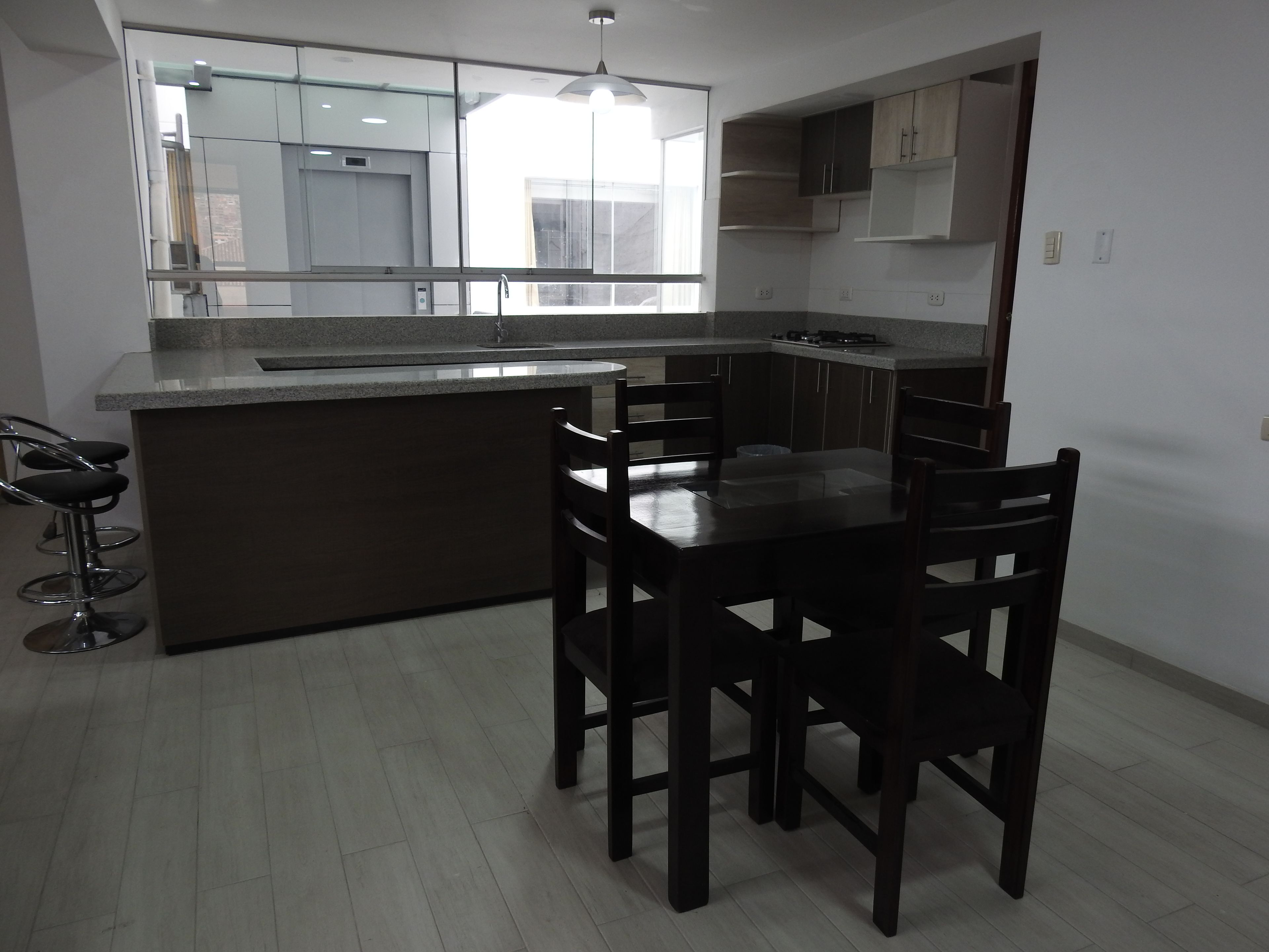 A modern kitchen with a central island, bar stools, and a dining table with chairs.