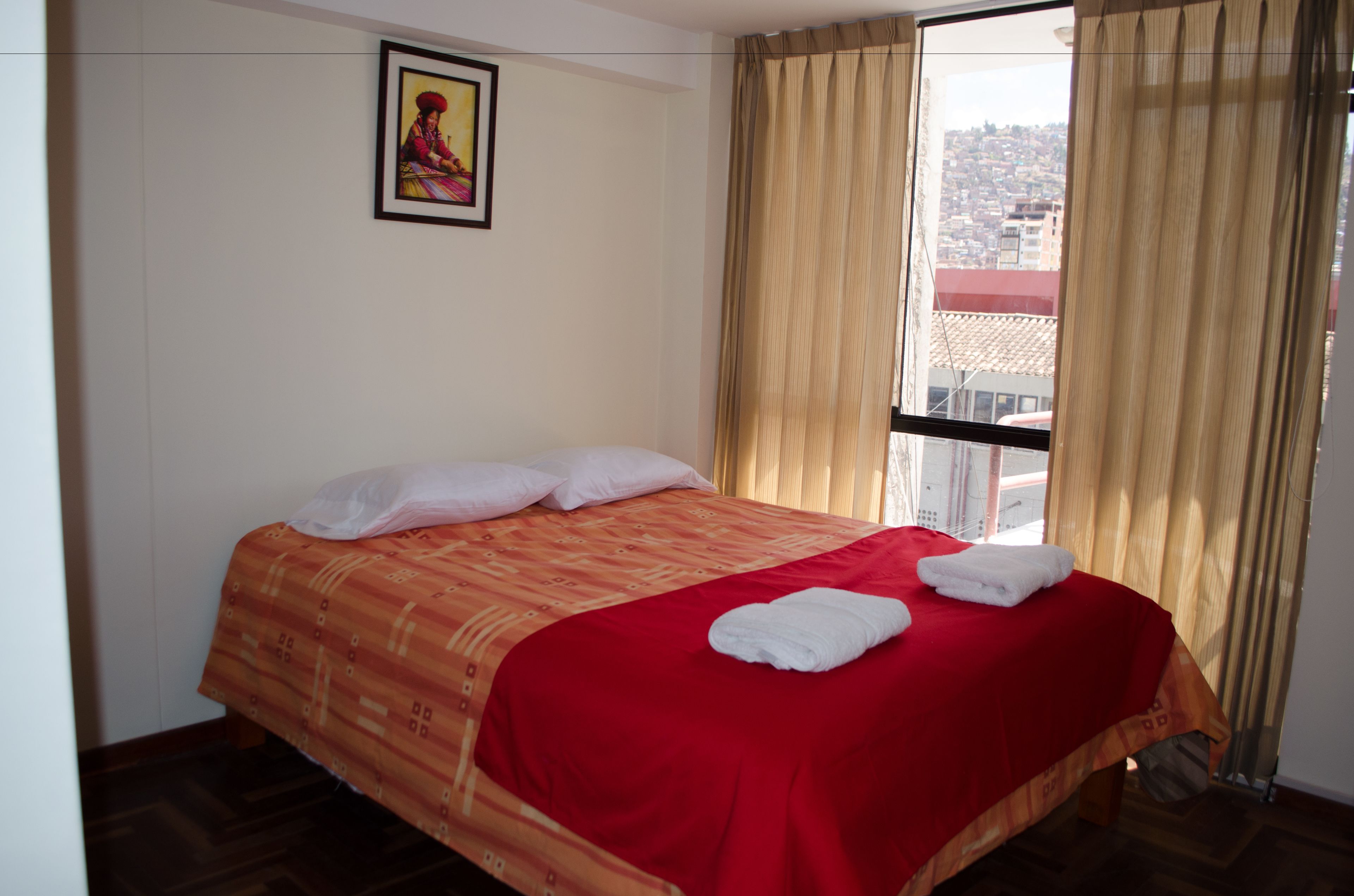 A hotel room with a bed, a window with curtains, and a framed picture on the wall.