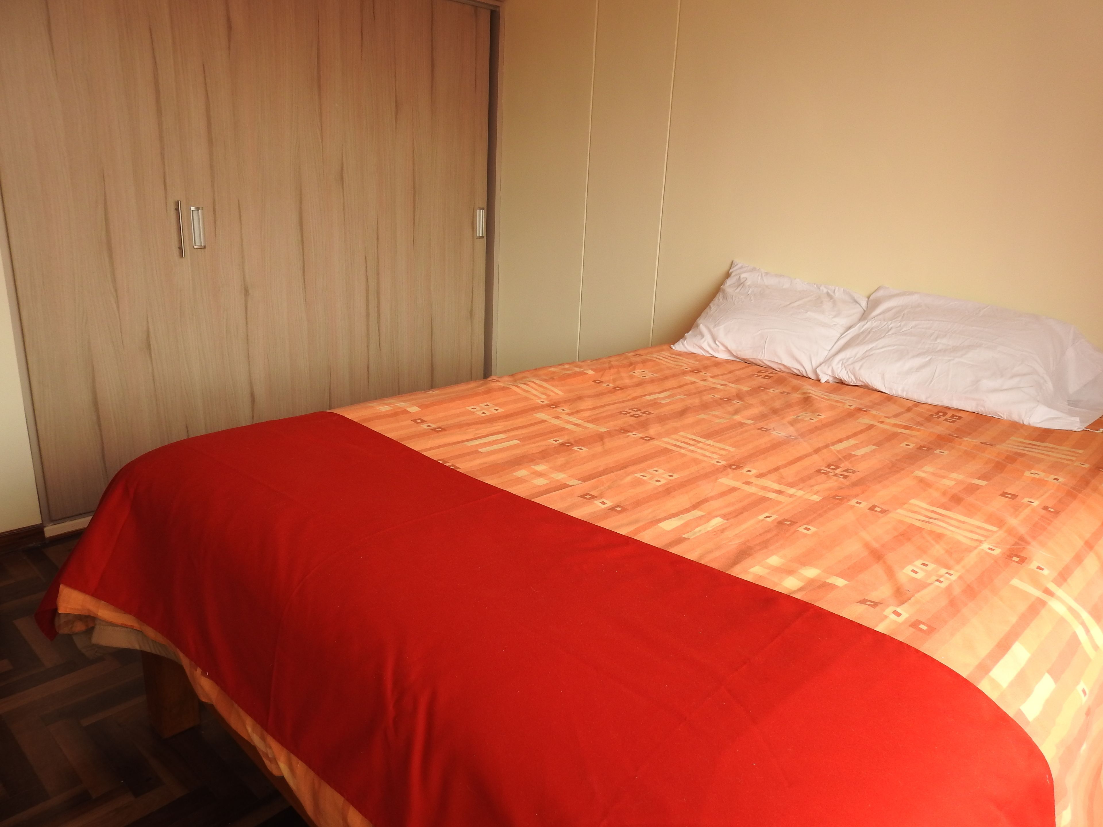 A bedroom with a bed, a wardrobe, and a plain wall.