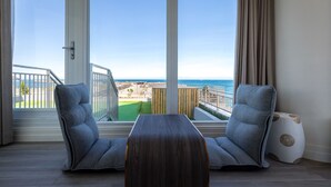 A modern room with a large window overlooking a coastal view, featuring two grey upholstered chairs and a wooden coffee table. - Brighthouse (Suao)