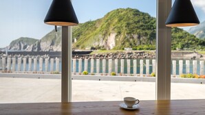 A table with a cup and saucer, two black lamps, and a view of a coastal landscape with mountains and a fence. - Brighthouse (Suao)