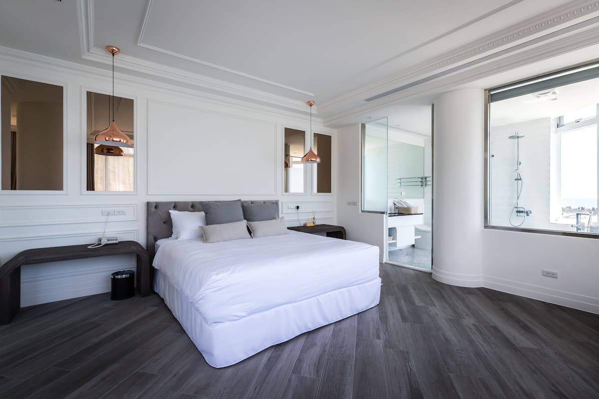 A modern hotel room with a large bed, two bedside tables, a large mirror, and a view of the bathroom.
