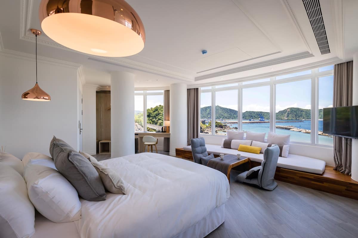 A hotel room with a large bed, a sofa, a desk, and a view of the sea.