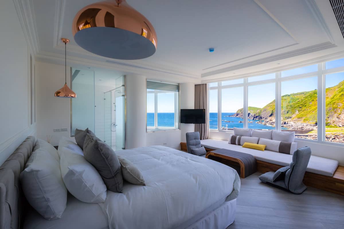 A modern hotel room with a large bed, seating area, and a view of the sea.