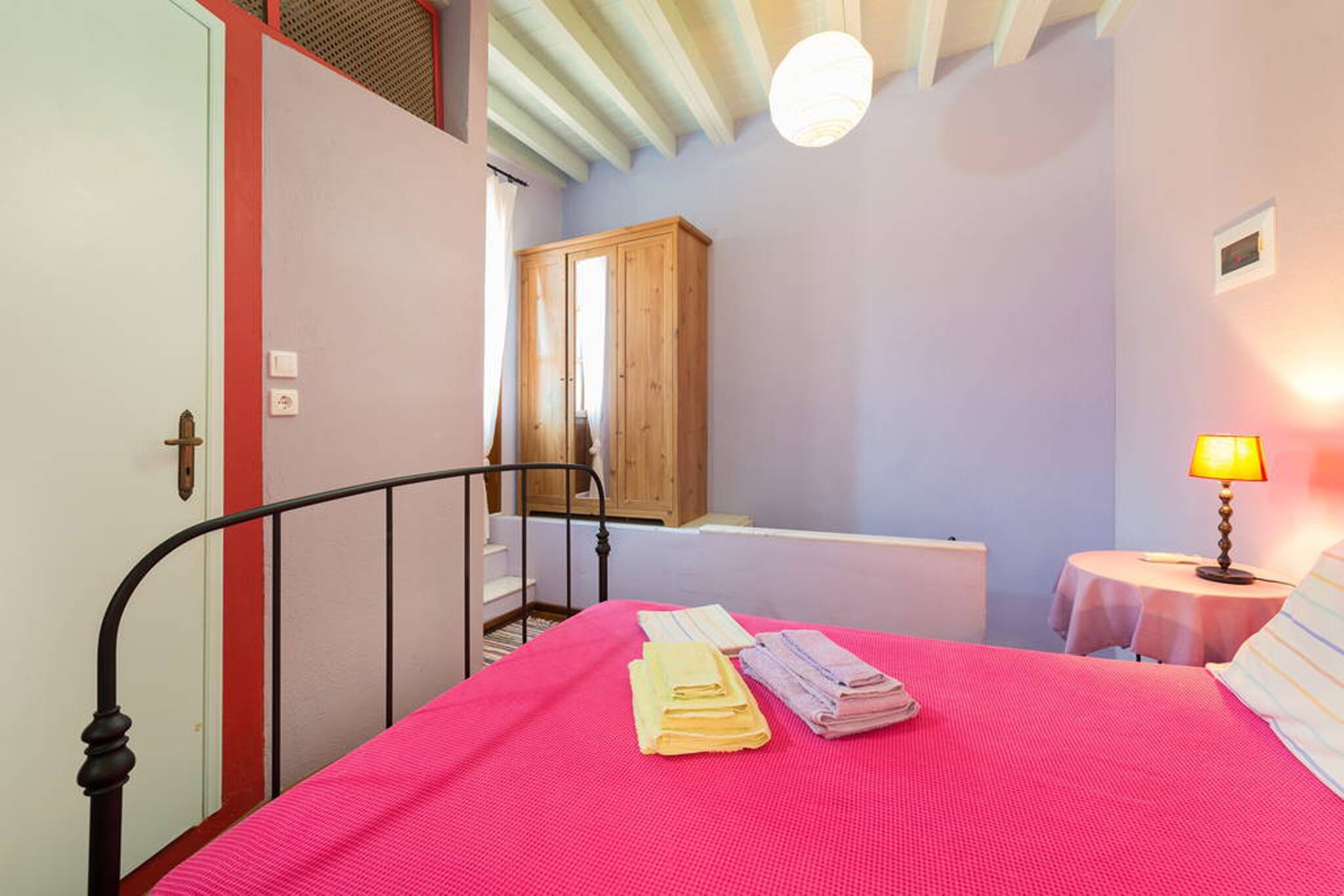 Un dormitorio con cama, un armario de madera, una mesa con lámpara y una escalera.