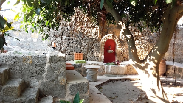 A stone courtyard with a red door, a small table, and a bench.