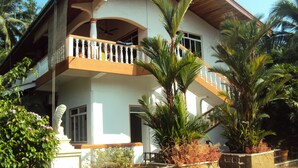 Une maison à deux étages dotée d’un balcon, entourée de plantes tropicales.