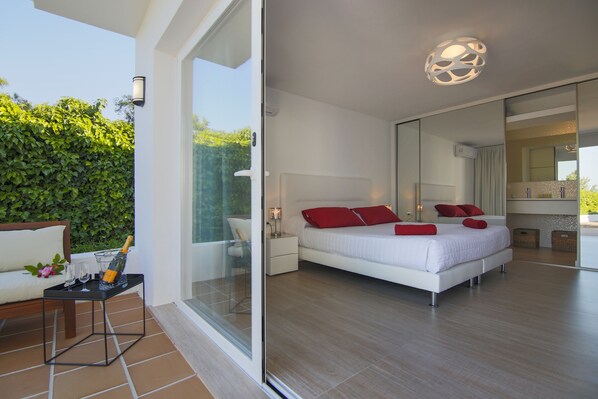 Une chambre moderne avec un grand lit, une porte vitrée donnant sur un balcon et une salle de bain avec un grand miroir.
