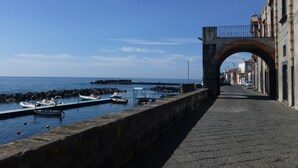 Un paseo marítimo con un arco de piedra, barcos amarrados en el muelle y edificios a lo largo del camino.
