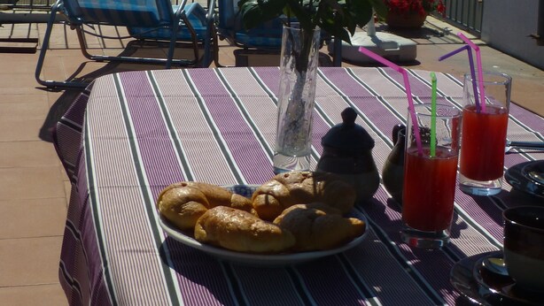 Una mesa con cruasanes, bebidas y un jarrón con flores en un balcón con vista al mar.