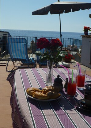 Una mesa con cruasanes, bebidas y un jarrón con flores en un balcón con vista al mar.