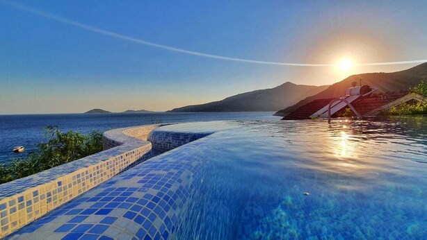 Une piscine à débordement offrant une vue dégagée sur la mer et les montagnes en arrière-plan.