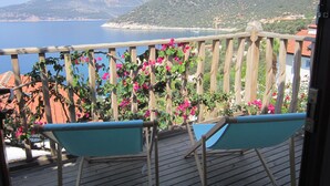 Un balcon avec une balustrade en bois, deux chaises bleues et des fleurs de bougainvillier roses.