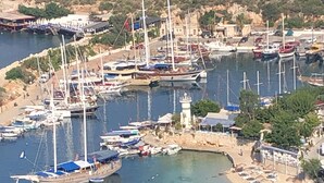 Un port de plaisance sur la côte, avec des bateaux amarrés, une plage de sable avec des parasols et un phare.