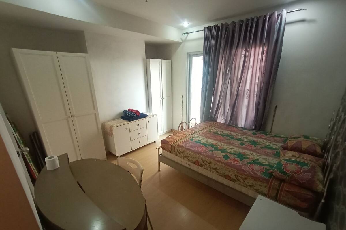 A bedroom with a bed, a desk, a chair, a wardrobe, and a window with curtains.