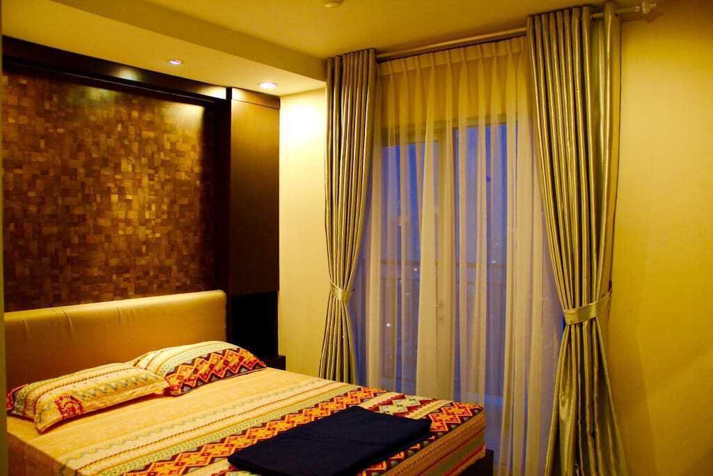 Ein Hotelzimmer mit einem großen Bett, einem Kopfteil, einem Fenster mit Vorhängen und einer Wand mit strukturierter Oberfläche.