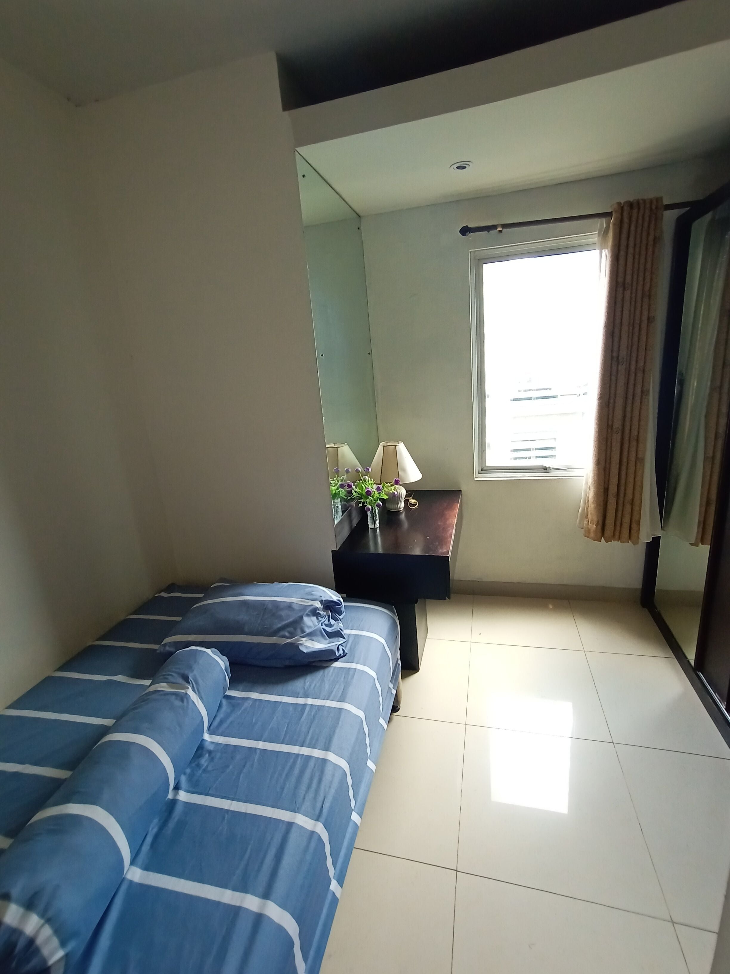 A bedroom with a bed, a nightstand, a lamp, and a window with curtains.