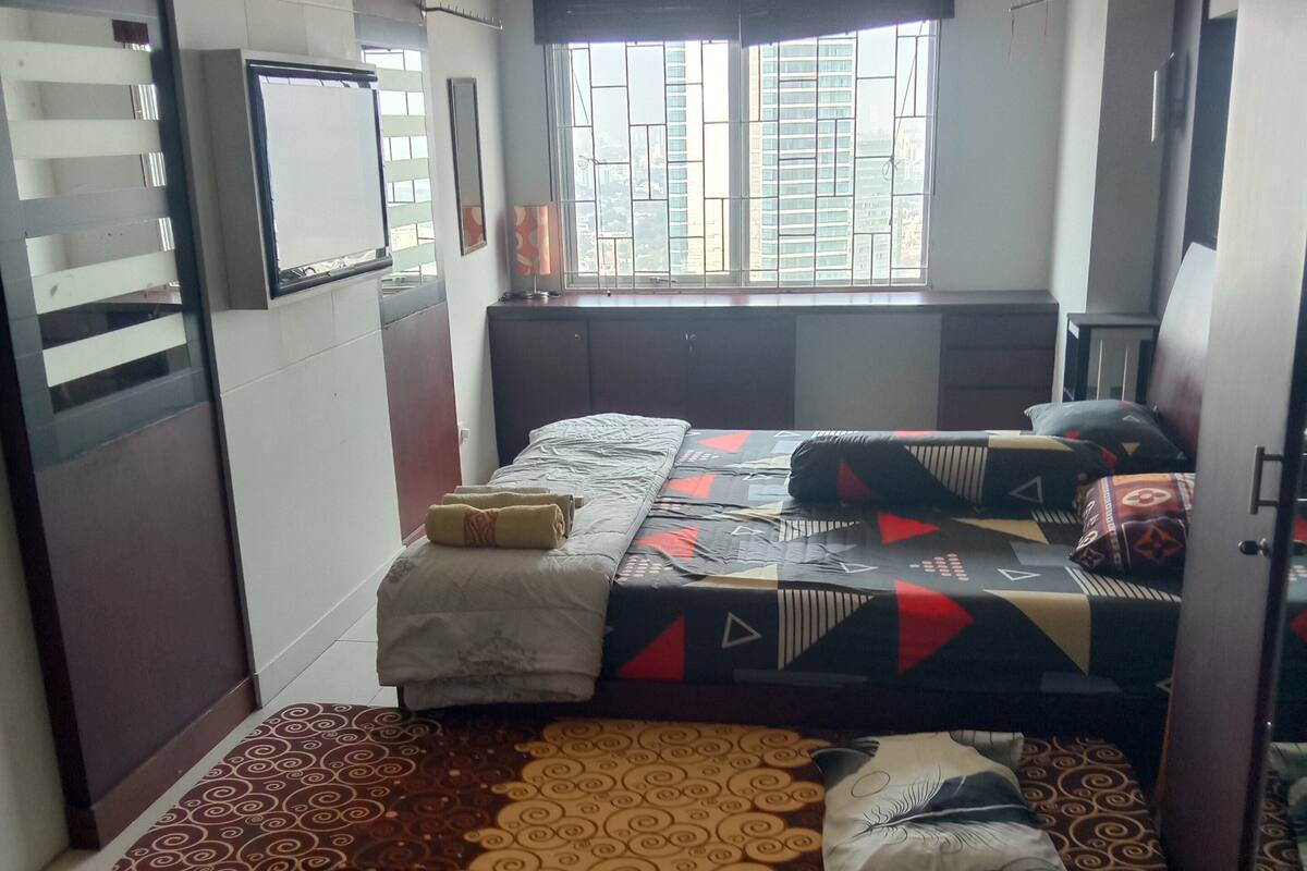 A bedroom with a bed, a window with bars, a clock, and a small table.