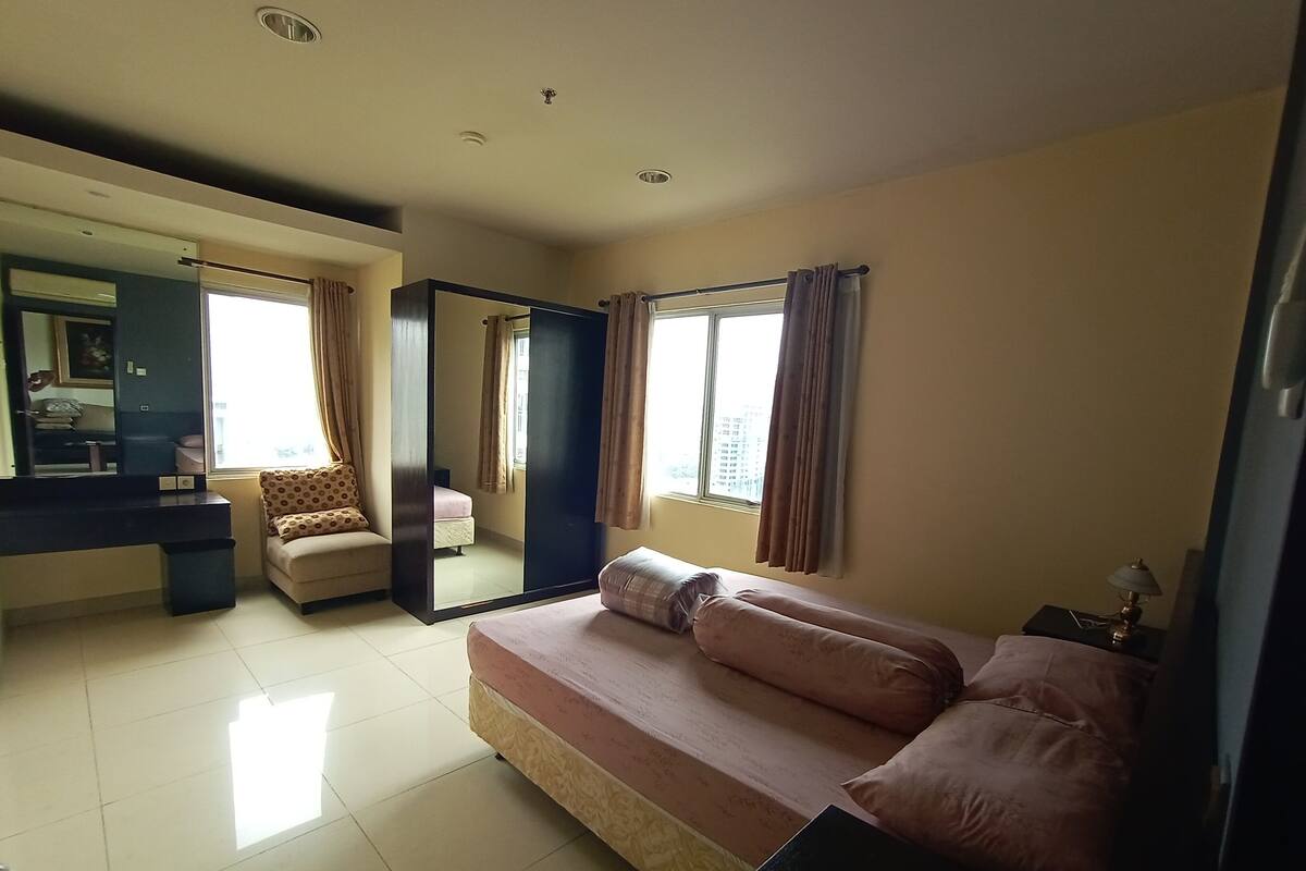 A bedroom with a bed, a dresser, a mirror, and a window with curtains.