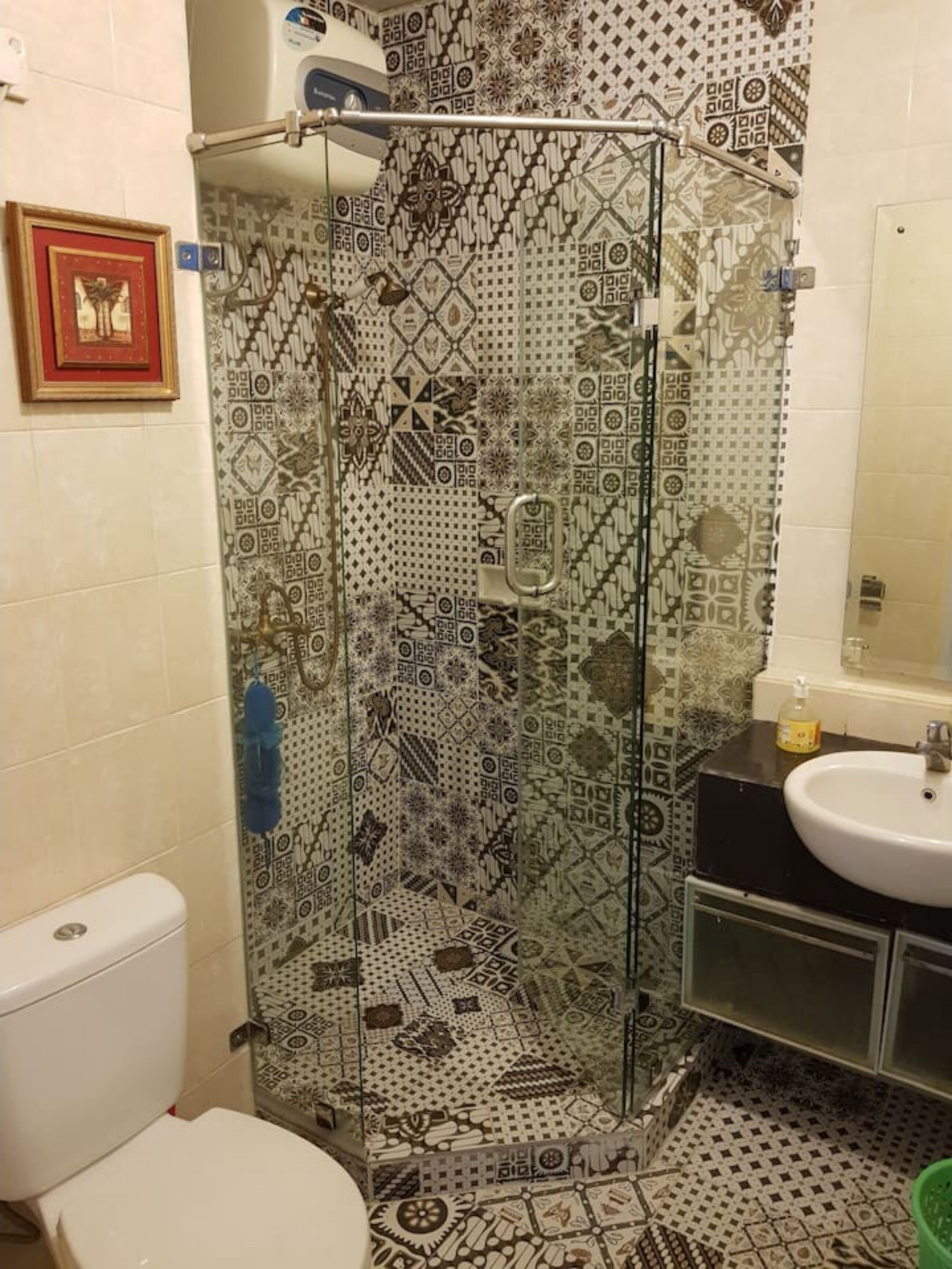 Une salle de bain avec un mur recouvert de carreaux décoratifs, une douche en verre, des toilettes et un lavabo avec un miroir.