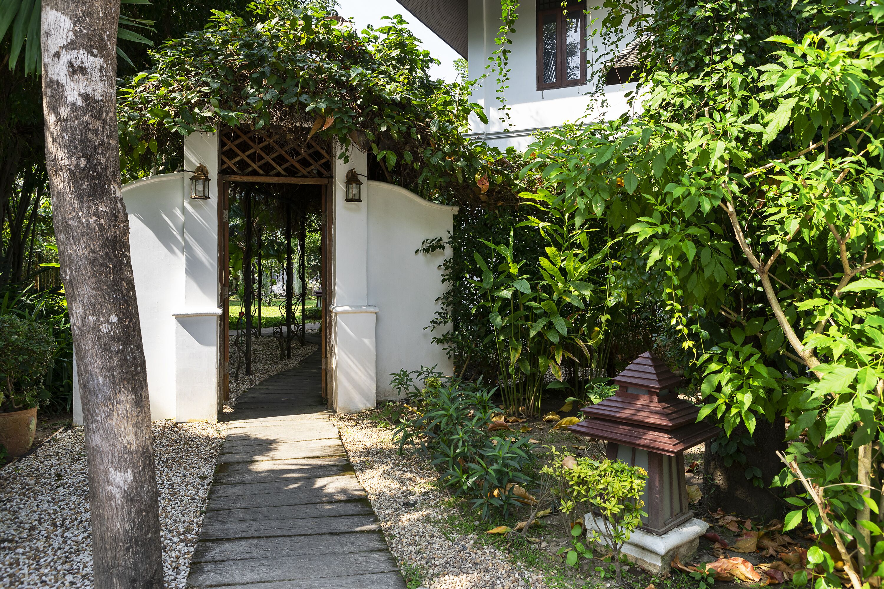 A pathway leading to a white building with a wooden gate and a small lantern.