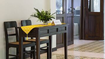 A dining area with a table set for two, a potted plant, and a view of the outside through a door.