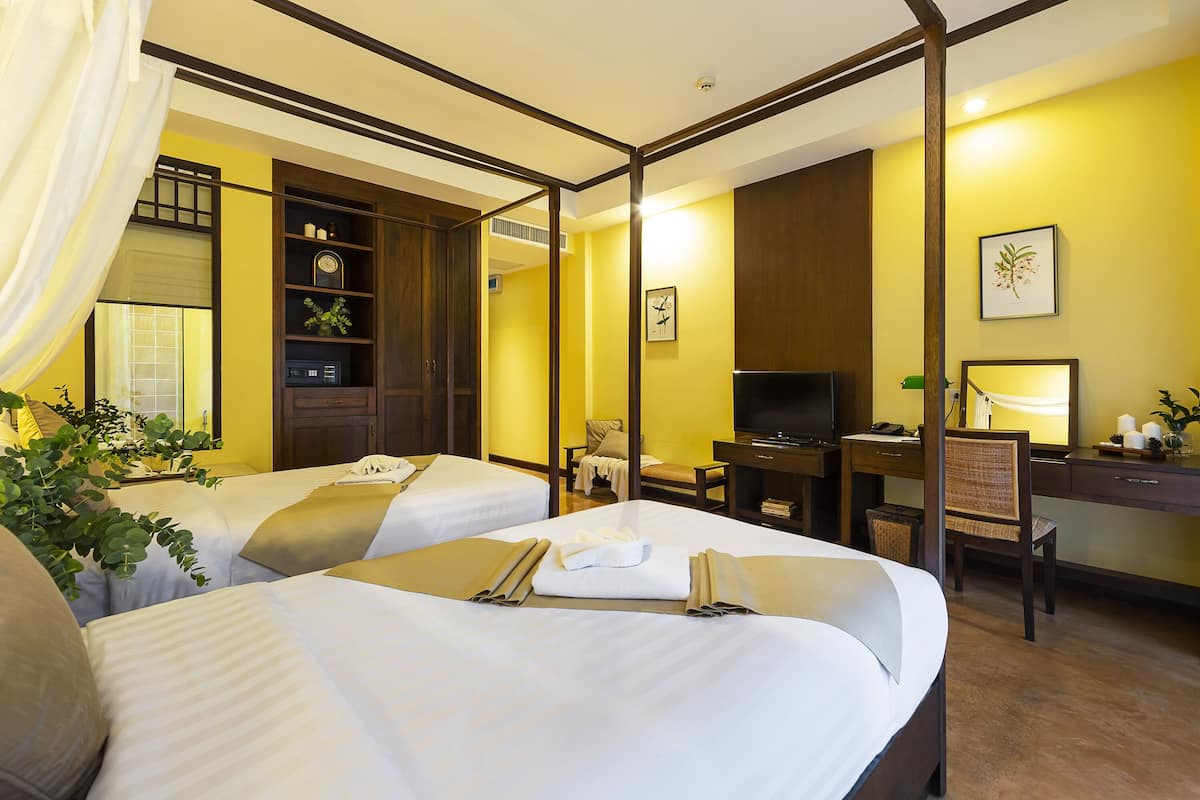 A hotel room with two beds, a desk, a chair, a television, and a bookshelf.
