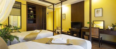 A hotel room with two beds, a desk, a chair, a television, and a bookshelf.