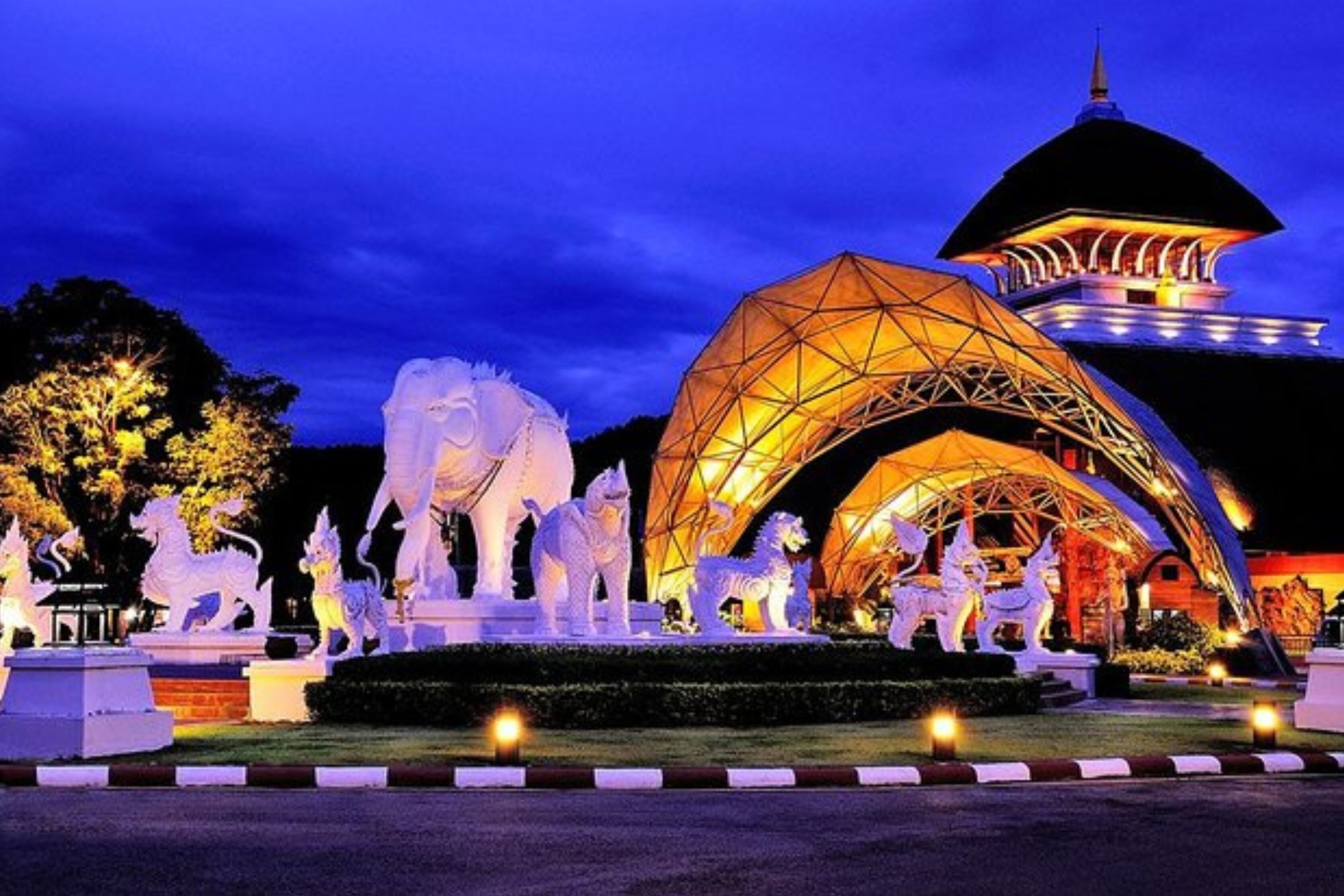 Vista nocturna de un edificio con una gran estructura en arco iluminada y estatuas de caballos blancos.