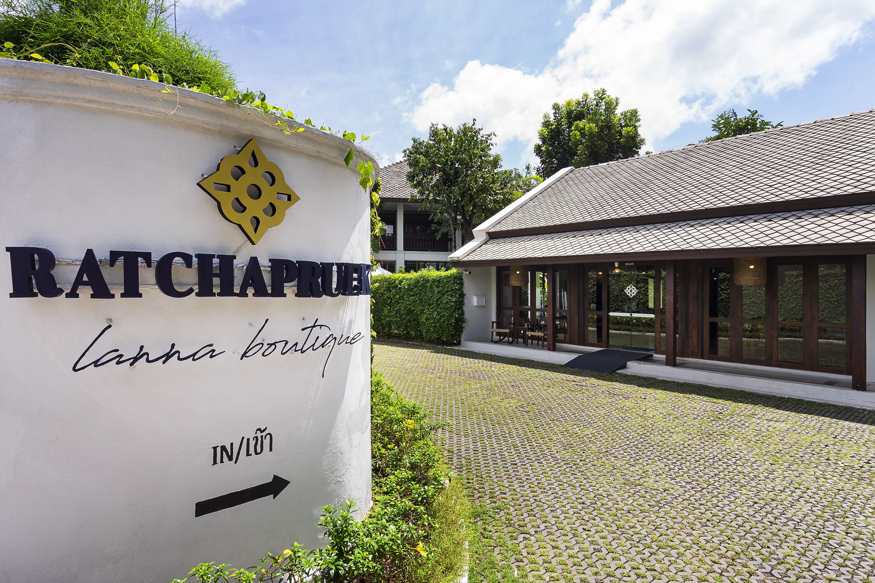 Un panneau indiquant la direction de Ratchaphrue, une flèche directionnelle, un chemin pavé et un bâtiment avec un toit en tuiles.