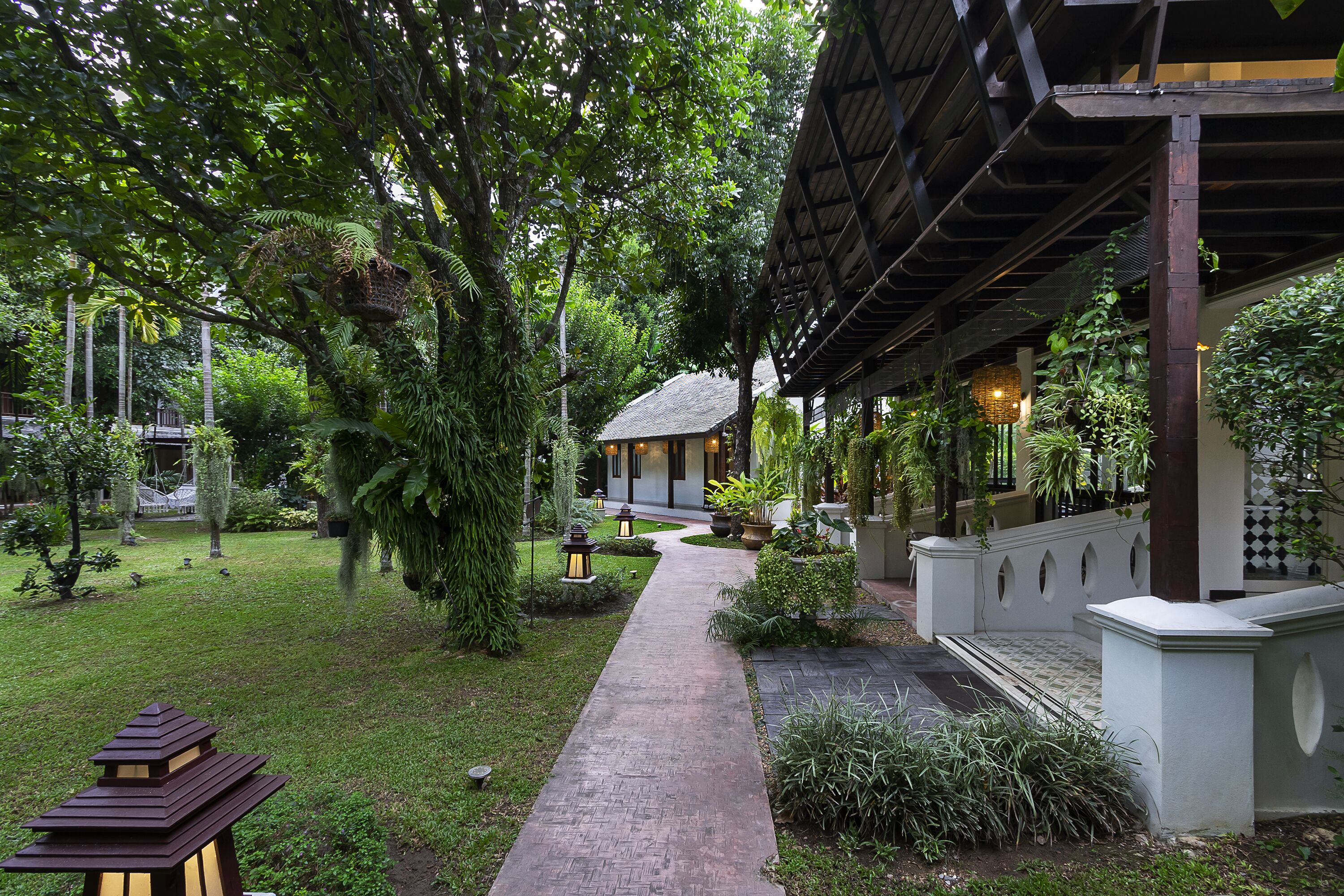 A pathway leading to a building with a covered porch, surrounded by lush greenery and a well-maintained garden.