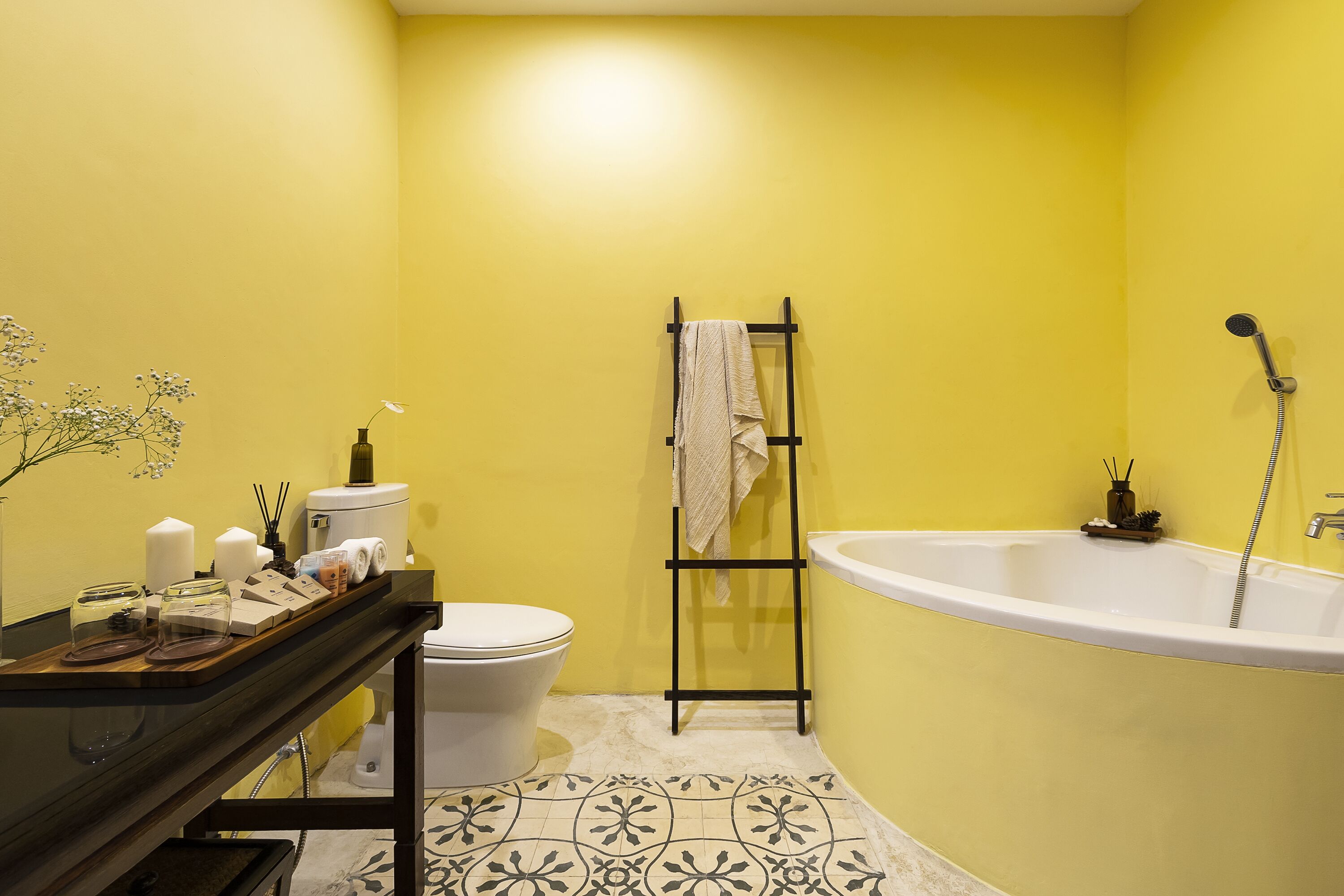 Un baño con una pared amarilla, una bañera blanca, un inodoro y un perchero para toallas.