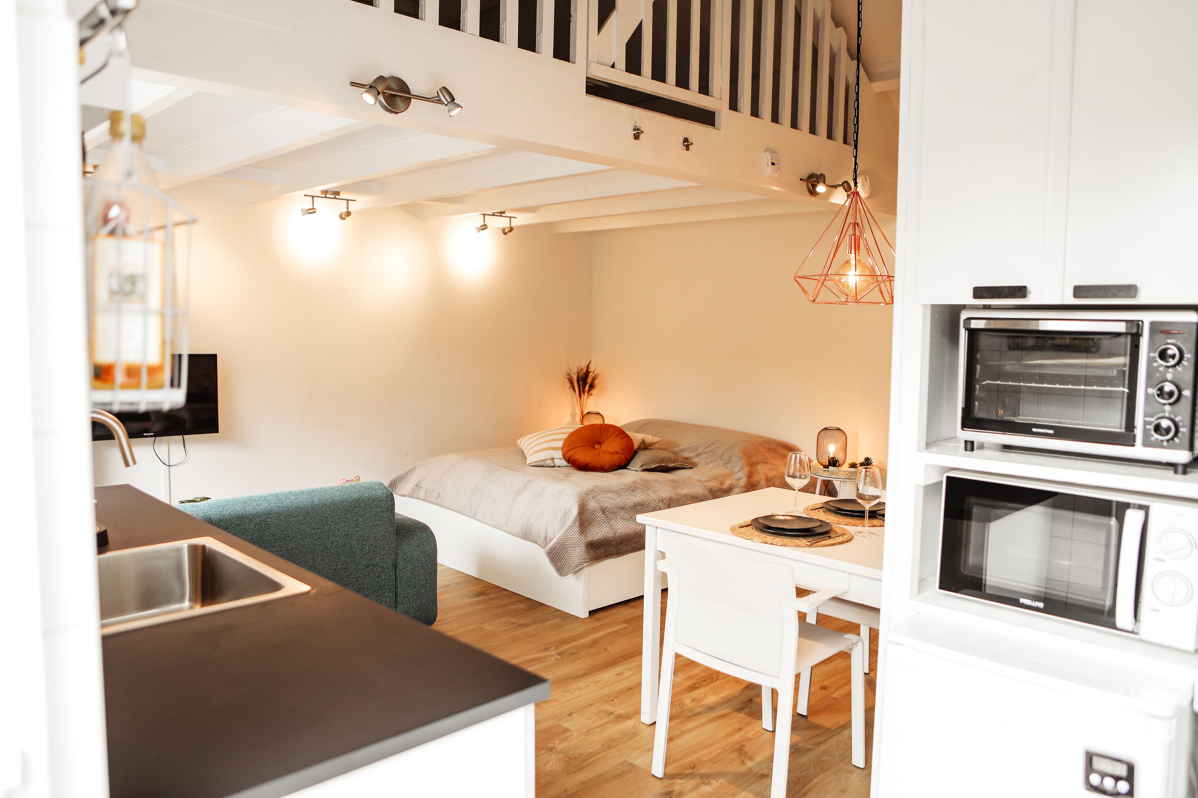 Une chambre compacte et moderne, équipée d’un lit, d’une petite table à manger, d’une kitchenette avec un évier et d’un four encastré.