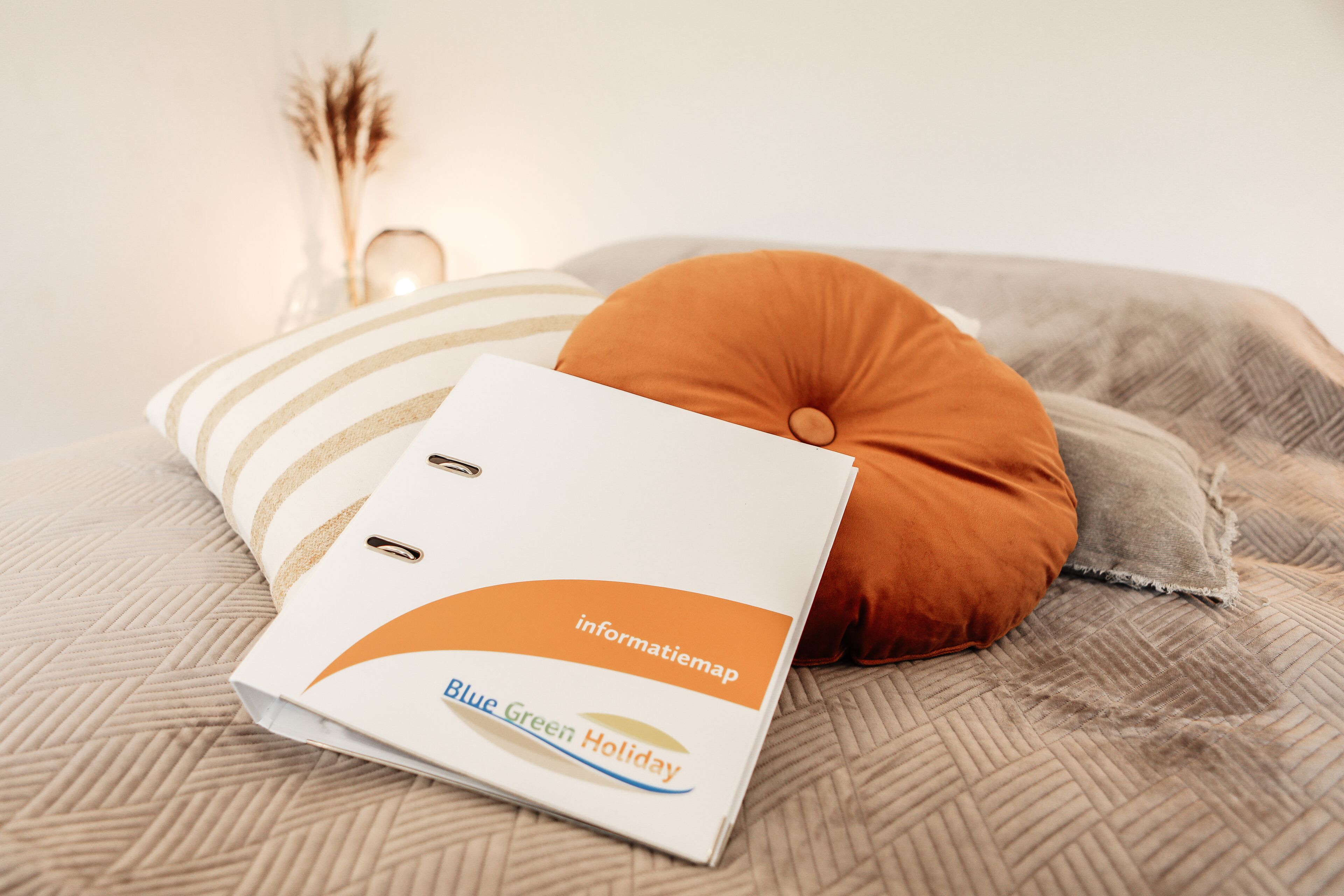 A neatly arranged bed with a white folder labeled "Blue Green Holiday" and a brown pillow.