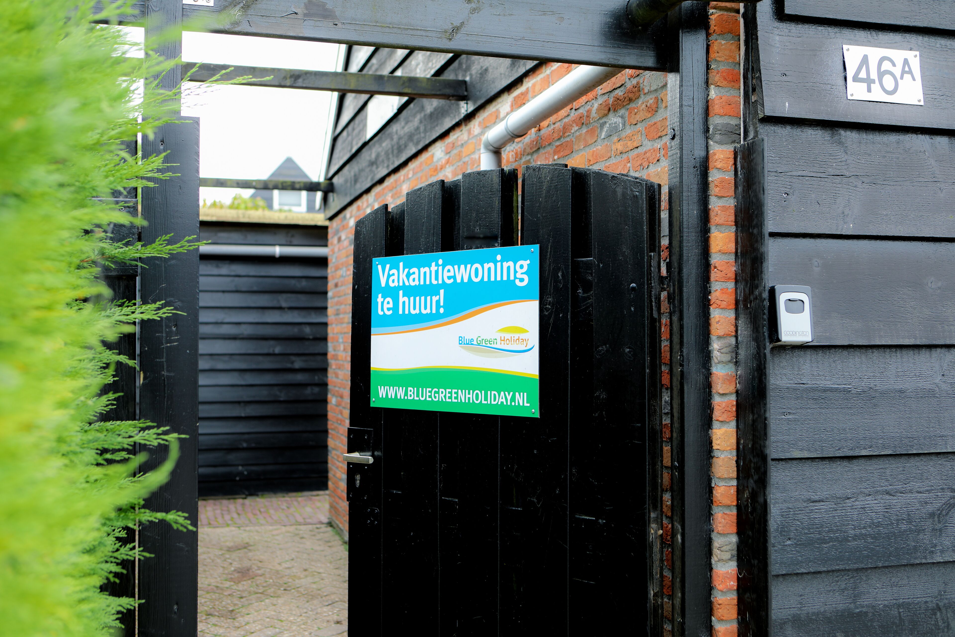 A black gate with a sign that reads 'Vakantiewoning te huur!' and a website address.