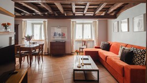 A living room with a wooden ceiling, a sofa, a coffee table, a TV, and a dining area with chairs and a table. - Elegant two-bedroom apartment in the very heart of Rome. Perfect for a family! (Roma)