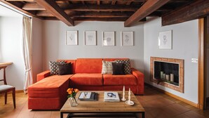 A living room with a wooden ceiling, a red sofa, a coffee table with books and candles, and a fireplace. - Elegant two-bedroom apartment in the very heart of Rome. Perfect for a family! (Roma)