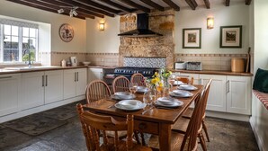A kitchen with a stone wall, wooden cabinets, a dining table set for four, and a vintage stove. - Pilgrim Cottage - sleeps 8 guests  in 4 bedrooms (Bourton-on-the-Hill)