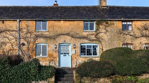 A traditional stone cottage with a blue door, multiple windows, and a sign reading "Pilgrim Cottage."