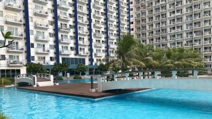 A swimming pool with a bridge, surrounded by palm trees and a high-rise building with balconies. - SM Jazz Residence by Good Rent (Makati)