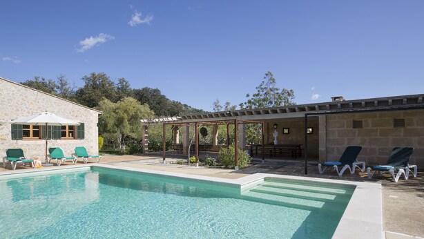 Piscina com espreguiçadeiras, pérgola e um edifício de pedra.