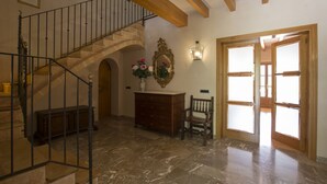 Um hall amplo com piso de mármore, escada de madeira, espelho decorativo e um banco.