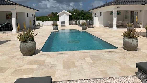 A swimming pool with a tiled deck, surrounded by potted plants and outdoor furniture. - Villa Sol, luxury fully equipped villa with wifi, a short distance from the sea (Kralendijk)