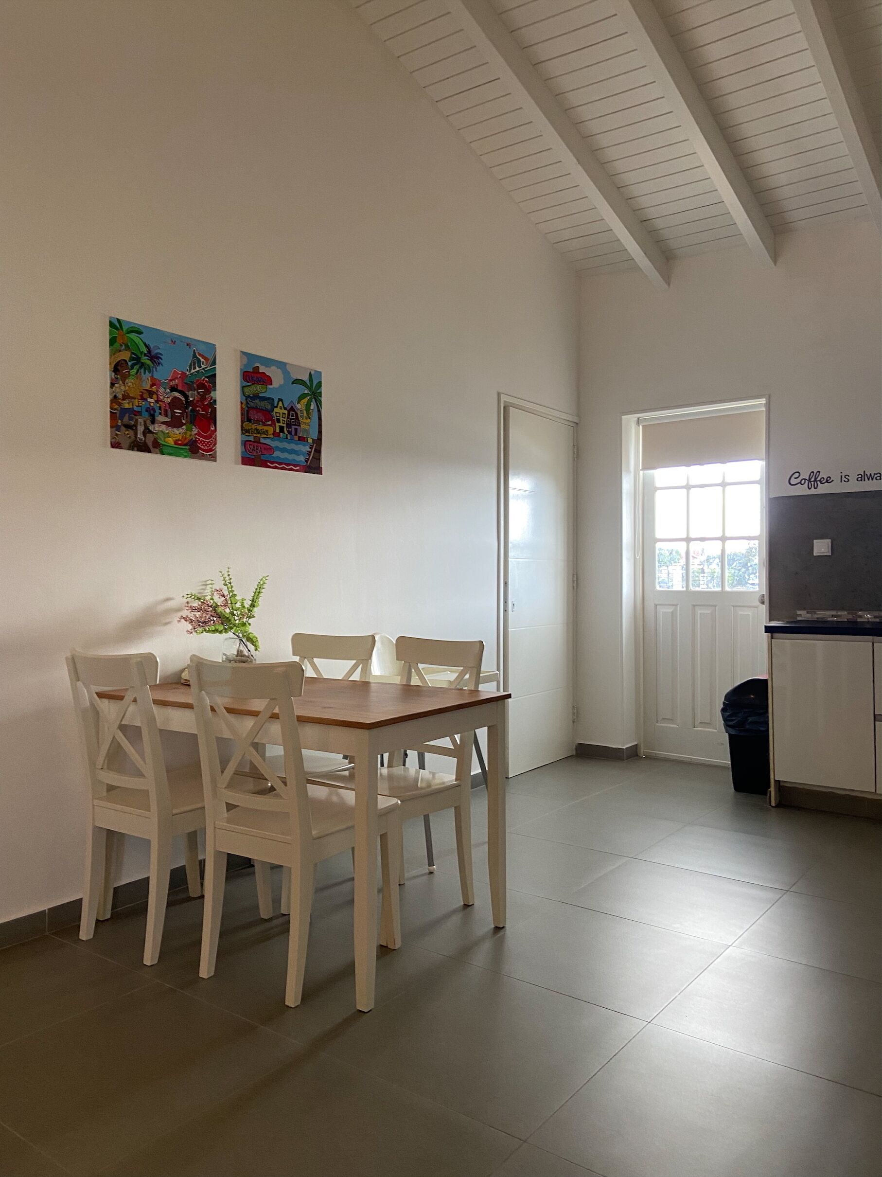 Un coin repas avec une table et des chaises, une petite plante et deux œuvres d’art colorées accrochées au mur.