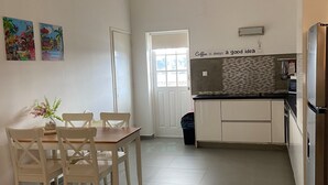 A kitchen with white cabinets, a tiled floor, and a dining area with a wooden table and chairs. There are two colorful paintings on the wall and a sign that says "Coffee is always a good idea." - Villa Sol, luxury fully equipped villa with wifi, a short distance from the sea (Kralendijk)