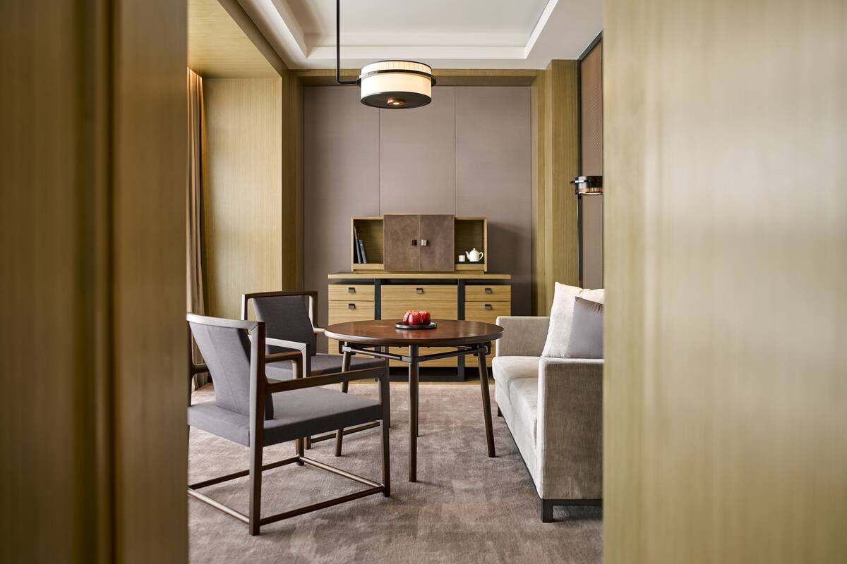A modern hotel room with a dining area, a sofa, and a cabinet with a tea set.