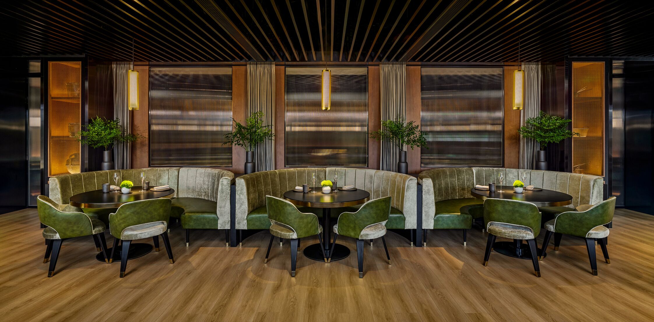 Un comedor moderno con suelo de madera, asientos tapizados en verde e iluminación colgante.