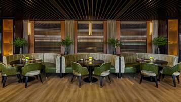 Un comedor moderno con suelo de madera, asientos tapizados en verde e iluminación colgante.