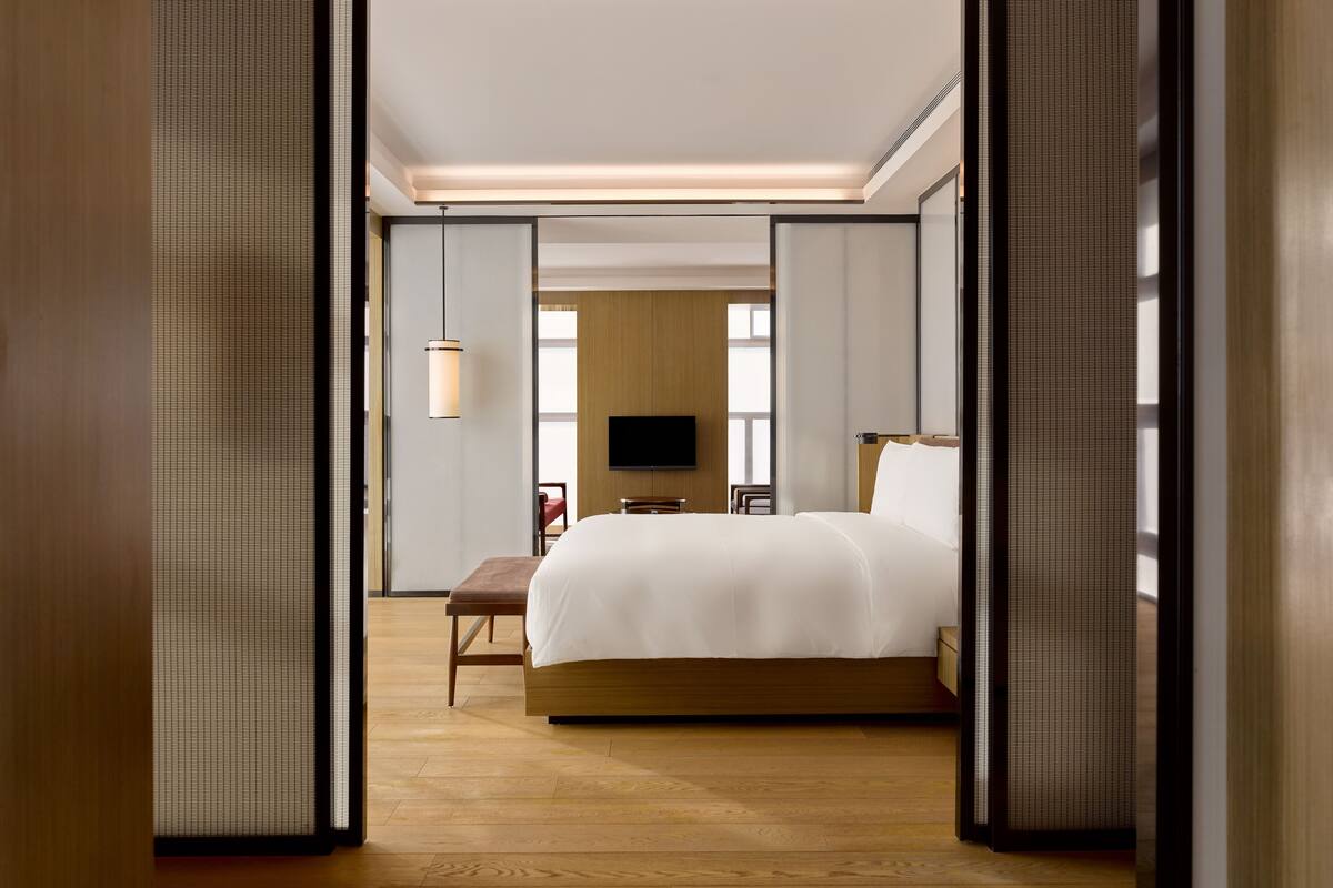 A modern hotel room with a large bed, a TV, and a wooden floor.